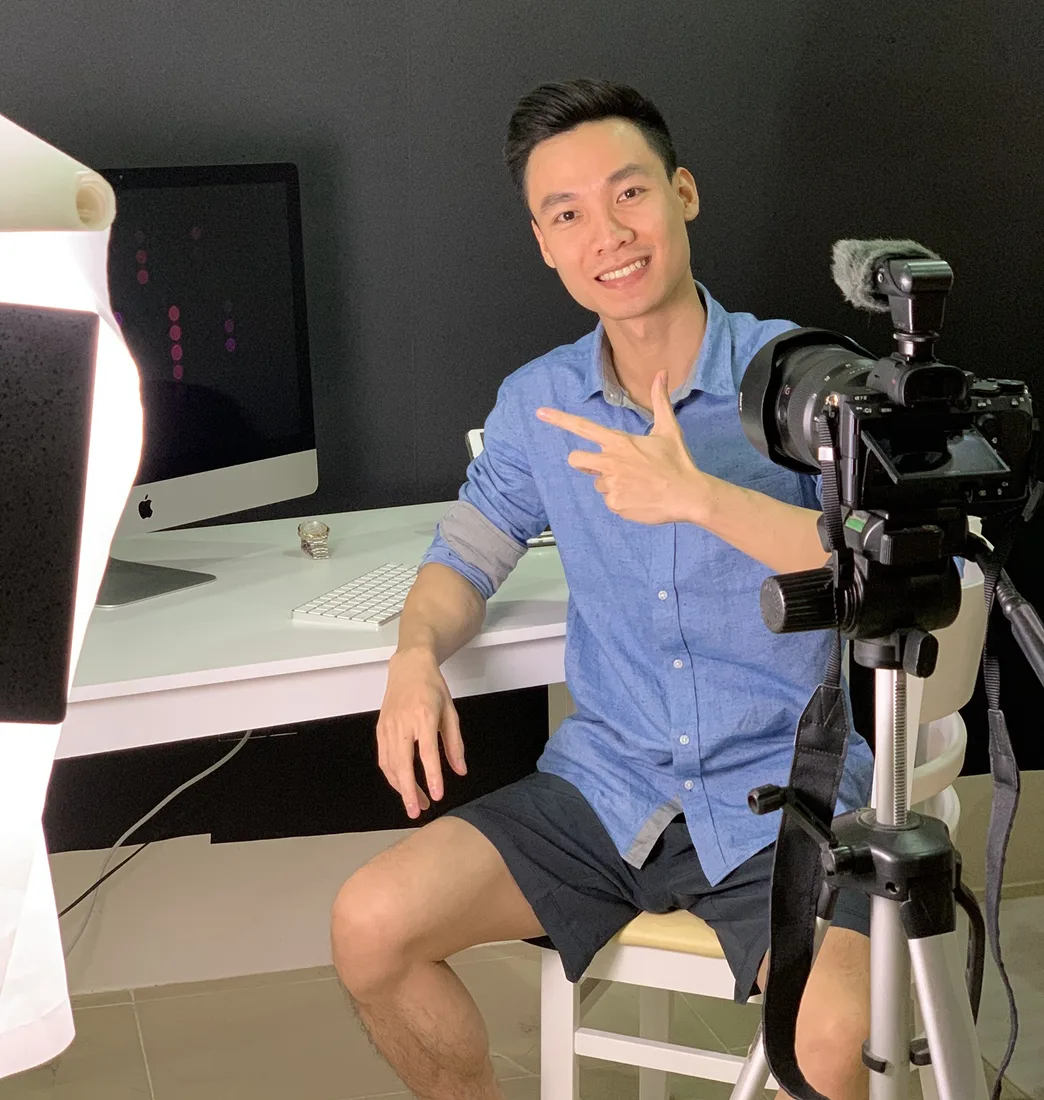 Tô Hải Đoàn ngồi quay video trước máy ảnh, mặc áo sơ mi xanh